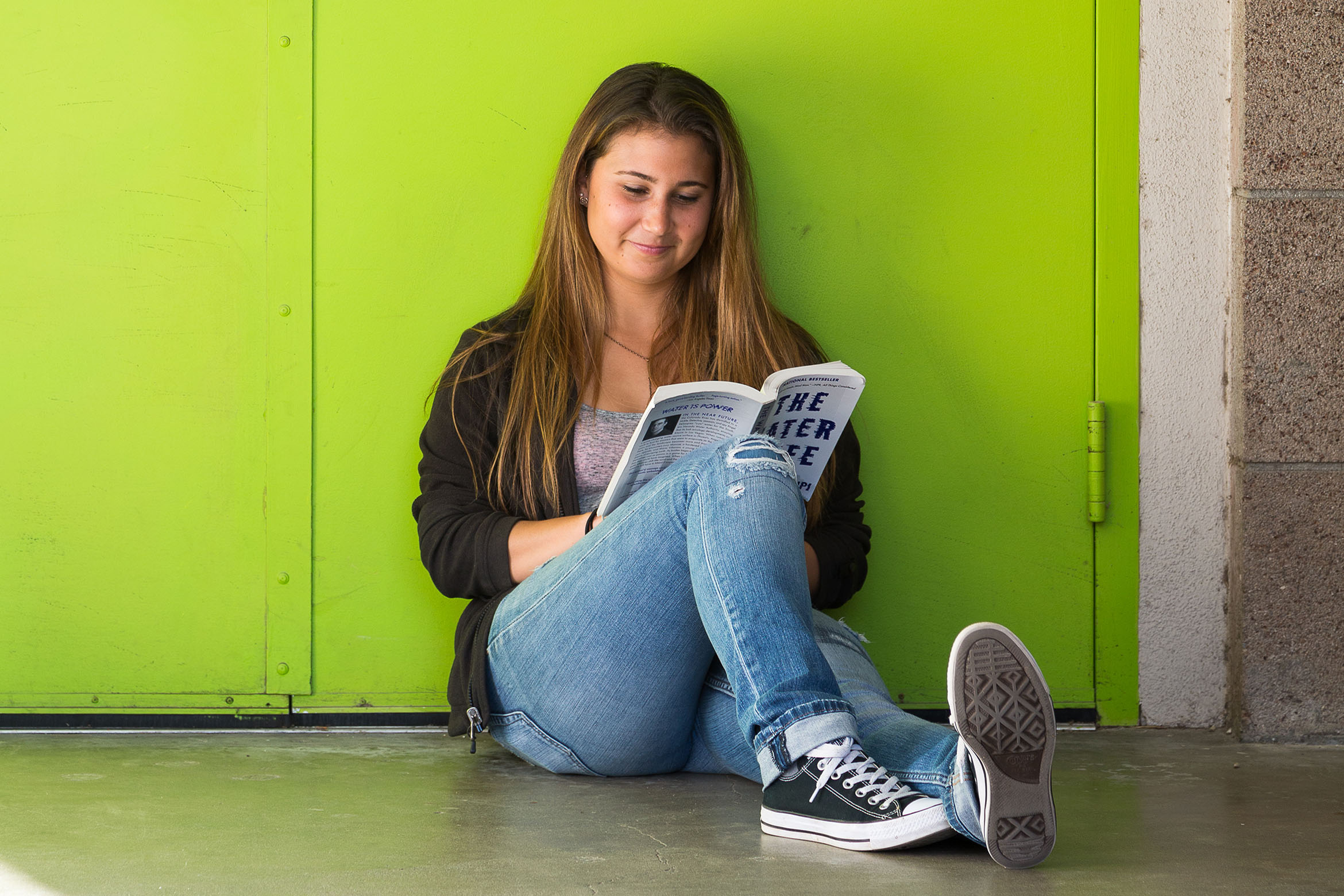 This is a student reading a book against a green wall.